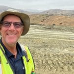 A man in hiking gear and a hat smiles at the camera.