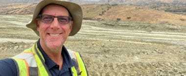 A man in hiking gear and a hat smiles at the camera.